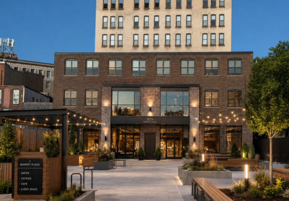Concept rendering of a redeveloped JB Wise site in downtown Watertown, New York, showing a modern plaza with landscaped walkways, seating areas, storefronts, and renovated brick architecture