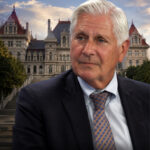 Bruce Blakeman in a suit posed before the New York State Capitol in Albany with WatertownPost.com branding at the bottom.