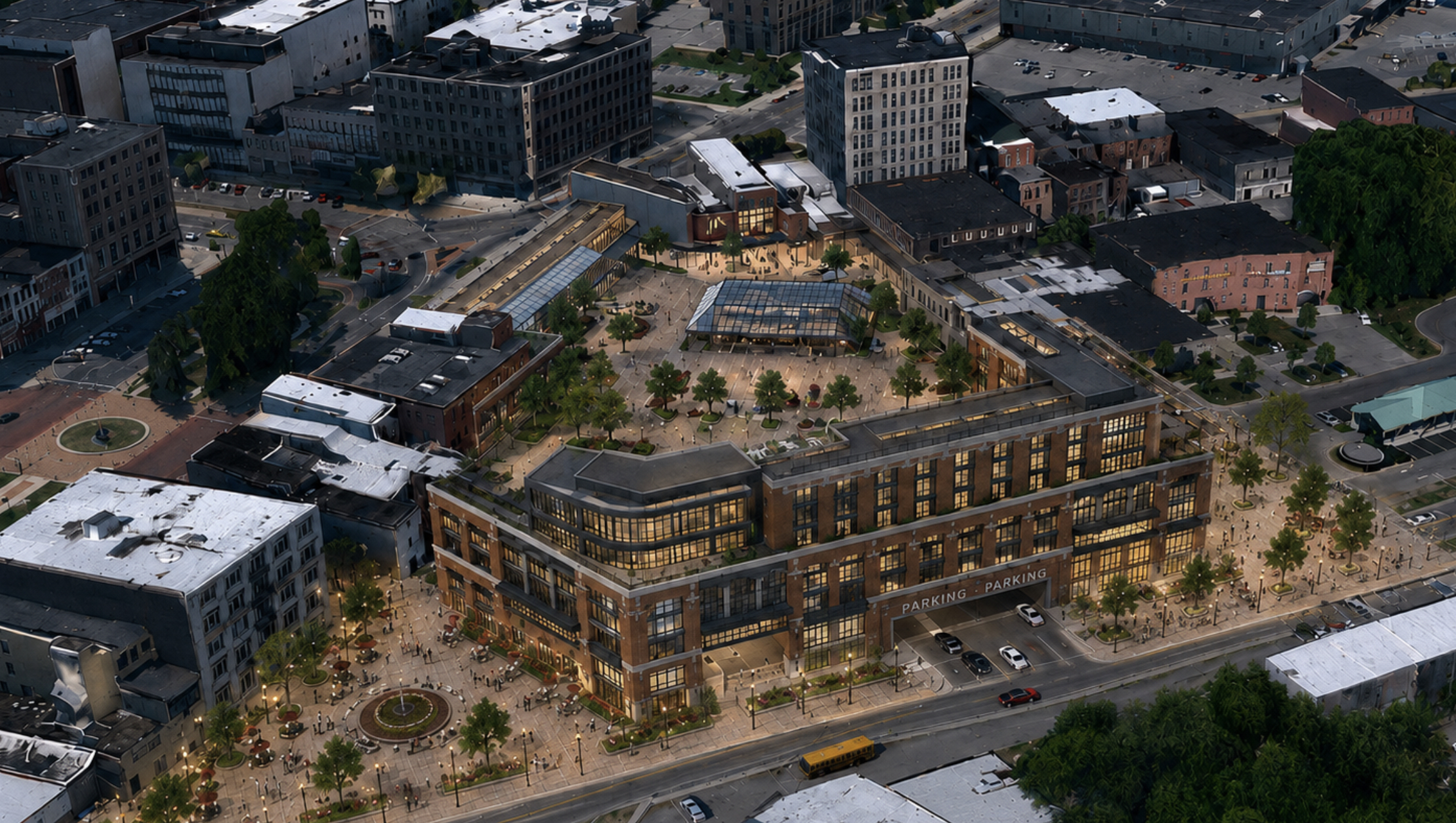 Aerial concept rendering of a modern mixed-use redevelopment in downtown Watertown, New York, showing a large brick-and-glass building surrounding an expansive public plaza with trees, seating, and walkways. The plaza extends around the east side of the building, while a roadway enters a ground-level parking garage integrated into the structure.