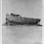 Historic photograph of the unfinished USS New Orleans, a massive War of 1812 ship-of-the-line, resting under its deteriorating shiphouse at Sackets Harbor, New York.