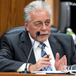 A suited city official speaks into a microphone while seated at a council desk with papers and glasses in front of him. A Watertown Post logo appears in the upper-right corner.