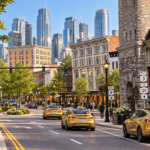 Concept image of downtown Watertown, New York, modernized with preserved historic buildings, landscaped streets, gold Tesla taxis, pedestrians, and tall glass skyscrapers rising in the background.