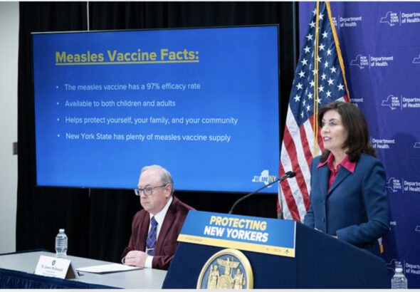 Governor Kathy Hochul speaks beside a display of measles vaccine facts during a New York State public health briefing.
